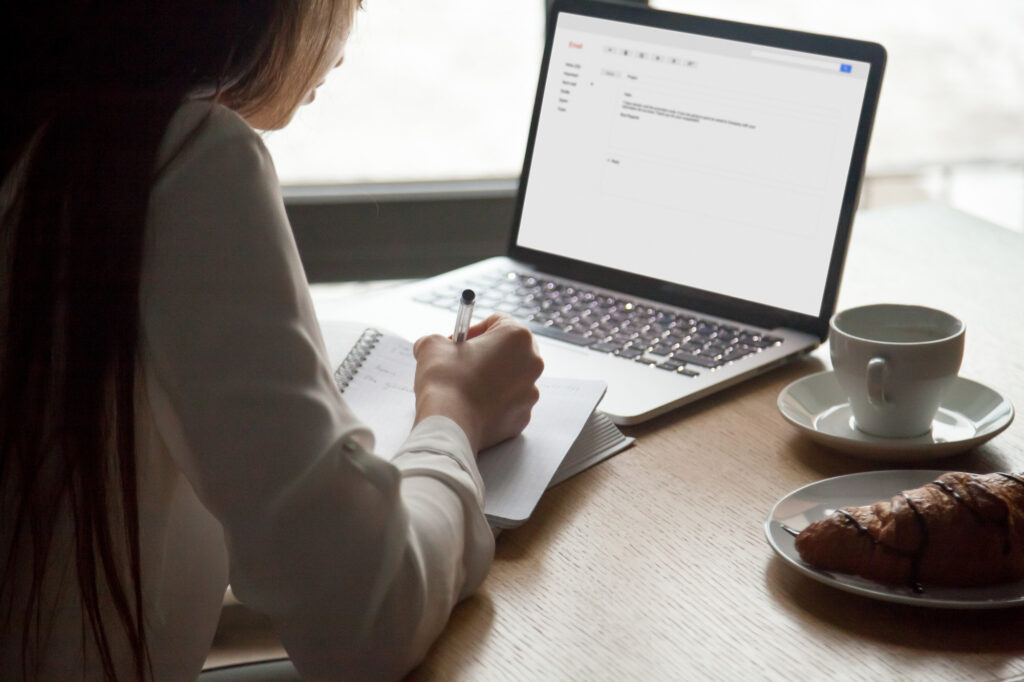 woman-making-notes-reading-email-letter-laptop-cafe